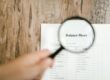 Close-up of a balance sheet document on wooden surface with a magnifying glass held by a hand.
