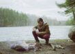 a man sitting next to a campfire near a lake
