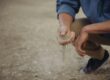 Person crouches down with a handful of sand that slips through their fingers